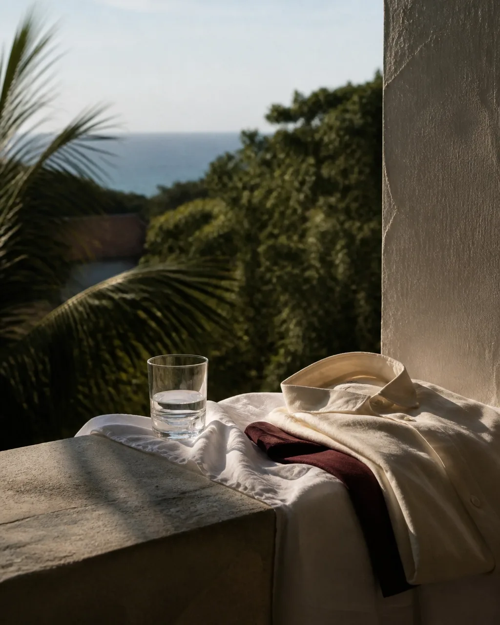 Mesa de verão com tecido branco, copo de água e paisagem costeira ao fundo